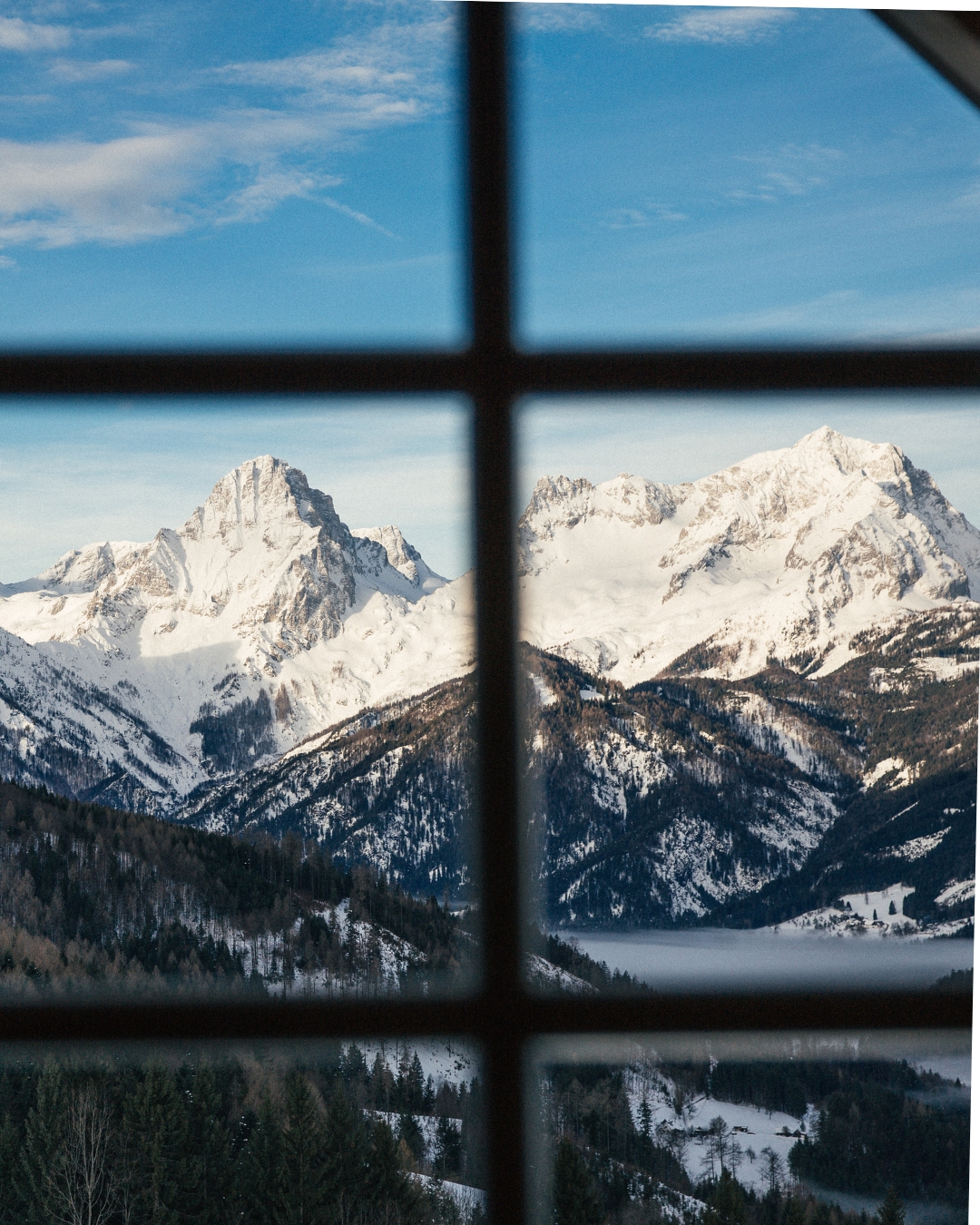 Blick durchs Fenster auf die verschneiten Berge